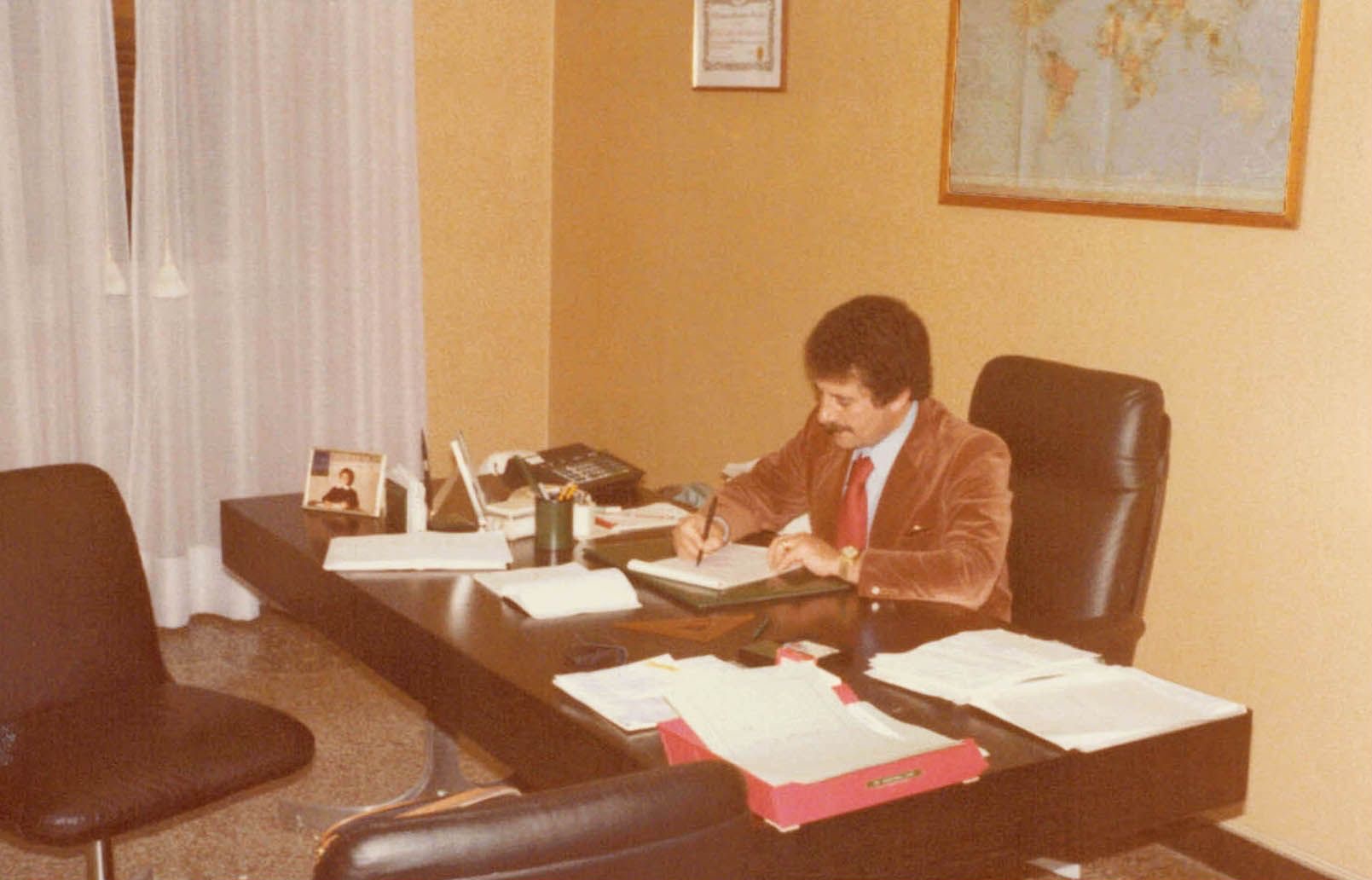 Filippo Giorgio Villa alla scrivania del suo ufficio, con giacca di velluto e cravatta rossa, mentre scrive