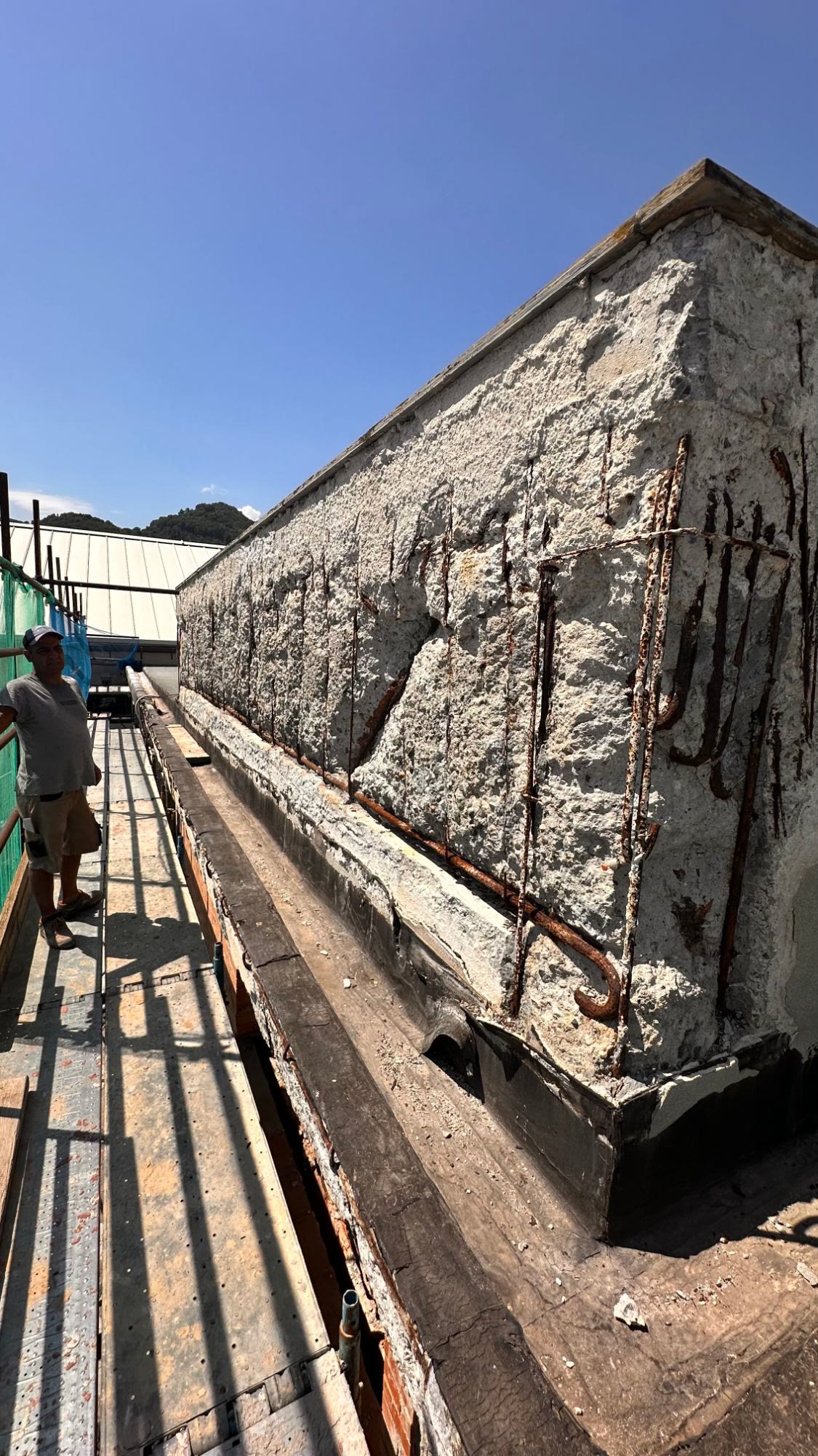 Il parapetto in cemento armato scrostato, con le staffe arrugginite a vista, e un operaio sul ponteggio