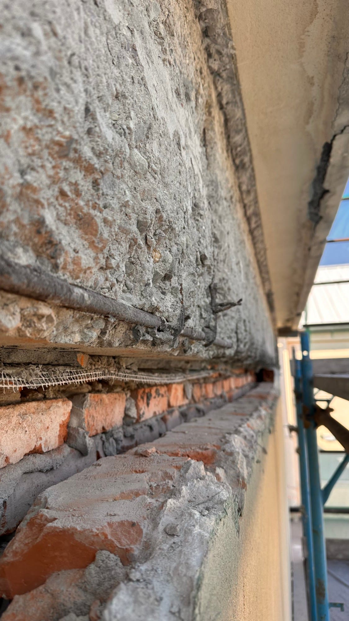 Una trave in cemento armato scrostata sopra la muratura in mattoni, vista di scorcio dal ponteggio