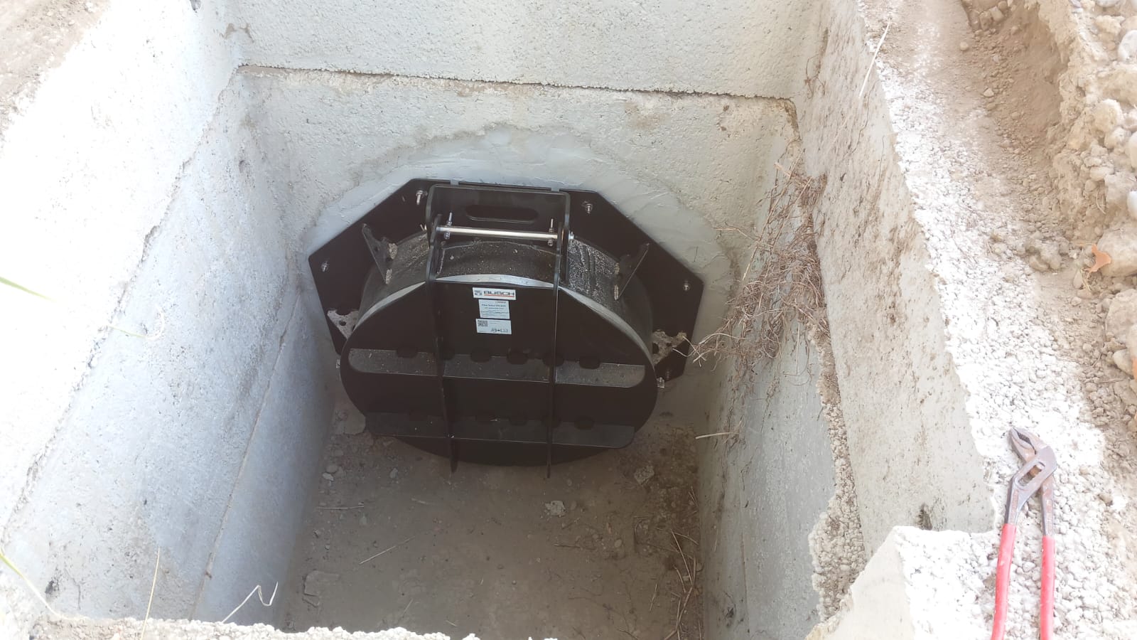 Una valvola a clapet nera fissata alla parete di un pozzetto in calcestruzzo