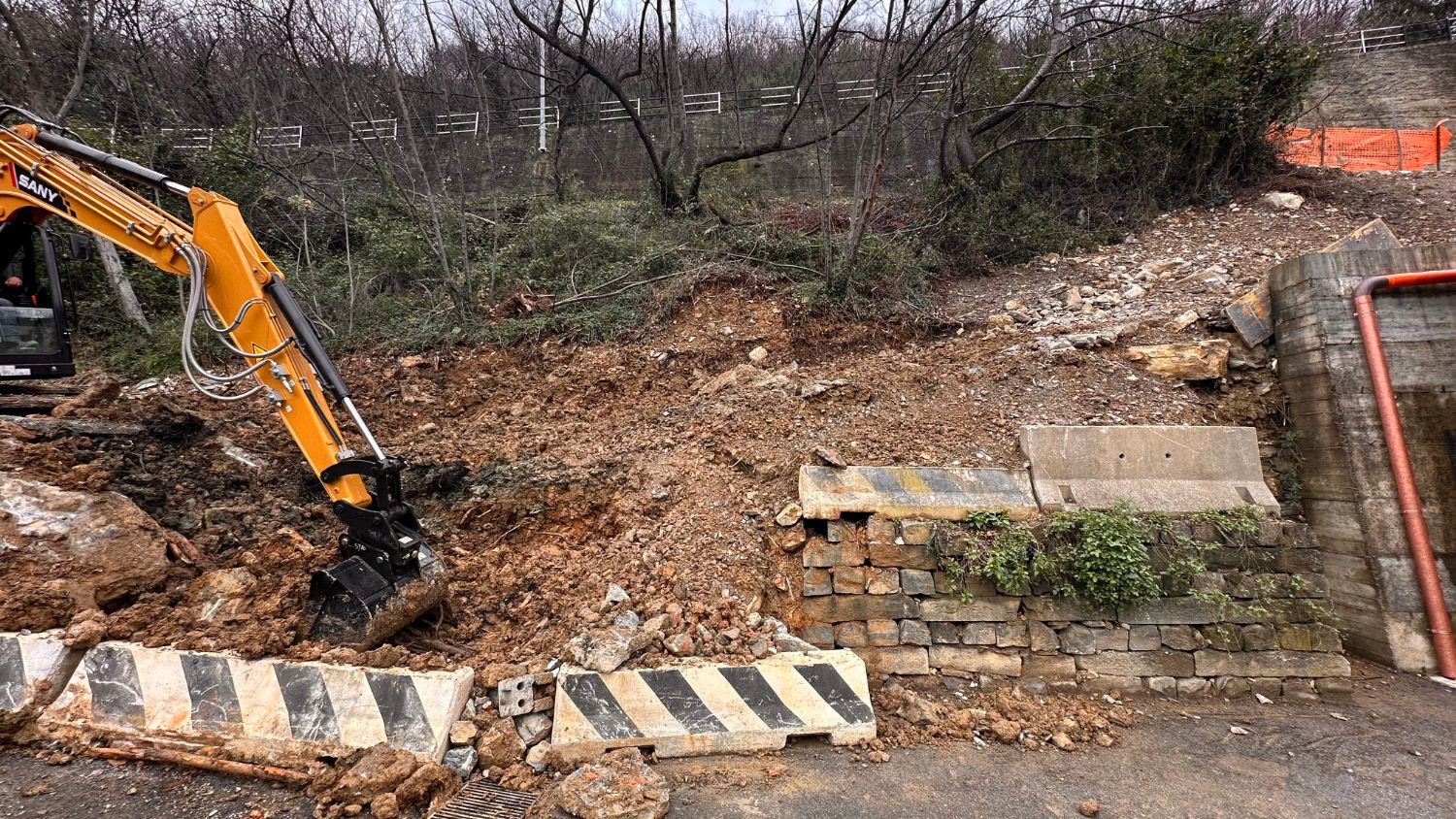 Il miniescavatore al lavoro sul pendio sopra la strada, accanto al vecchio muretto in pietra