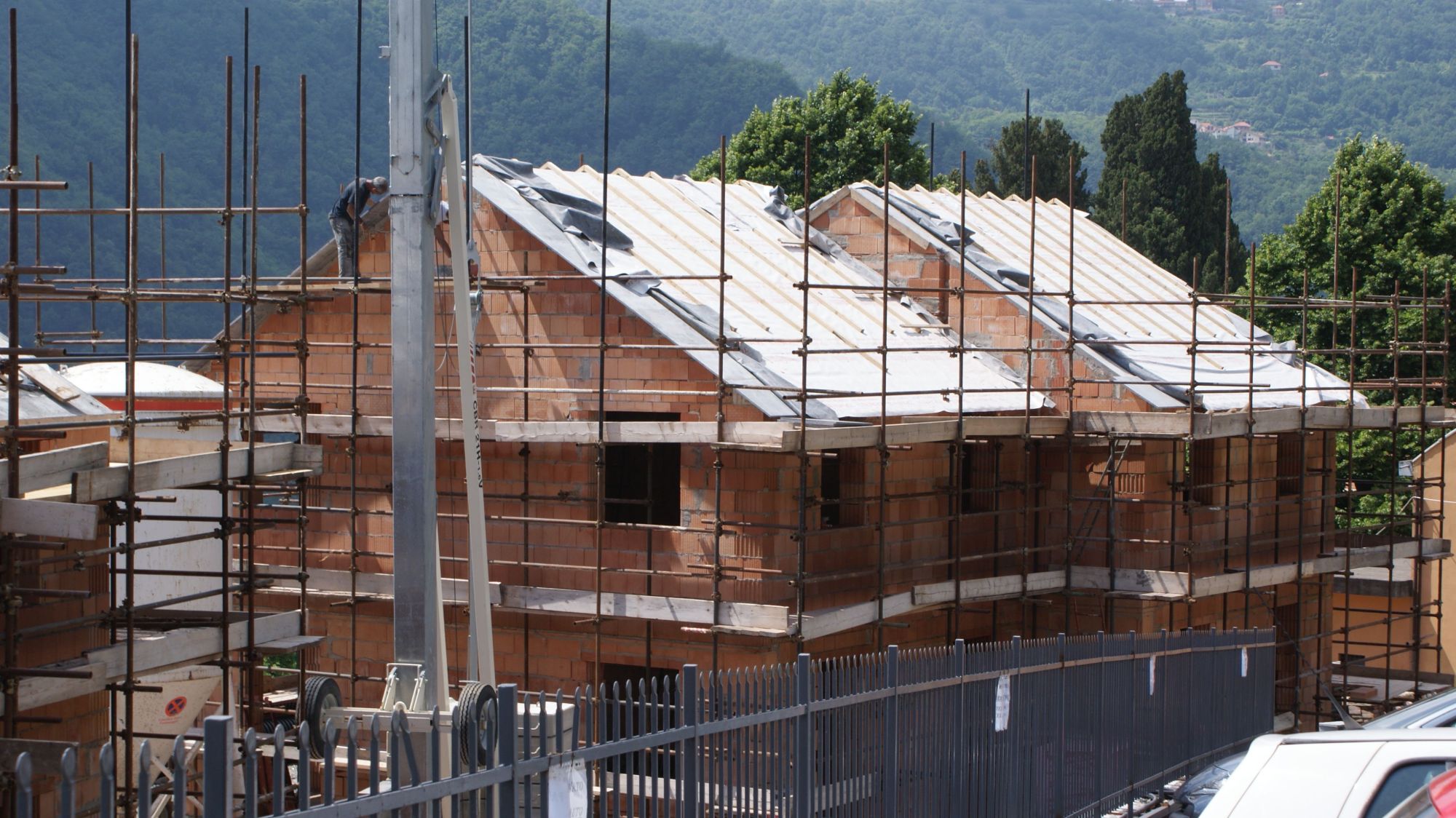 Una palazzina con i muri in laterizio e il tetto in legno coperto dal telo, fra i ponteggi