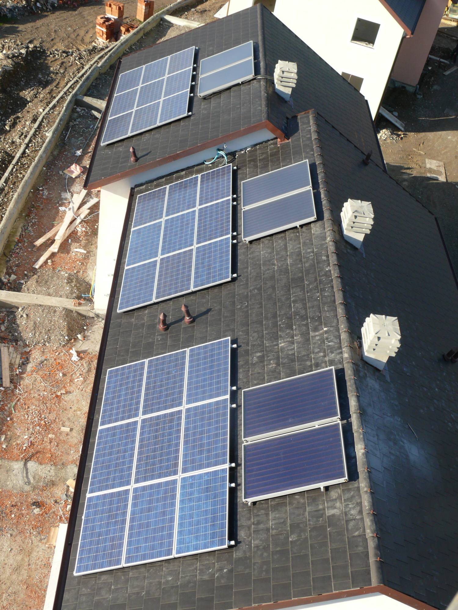 Un tetto visto dall'alto con tre gruppi di pannelli fotovoltaici e, accanto, i collettori del solare termico