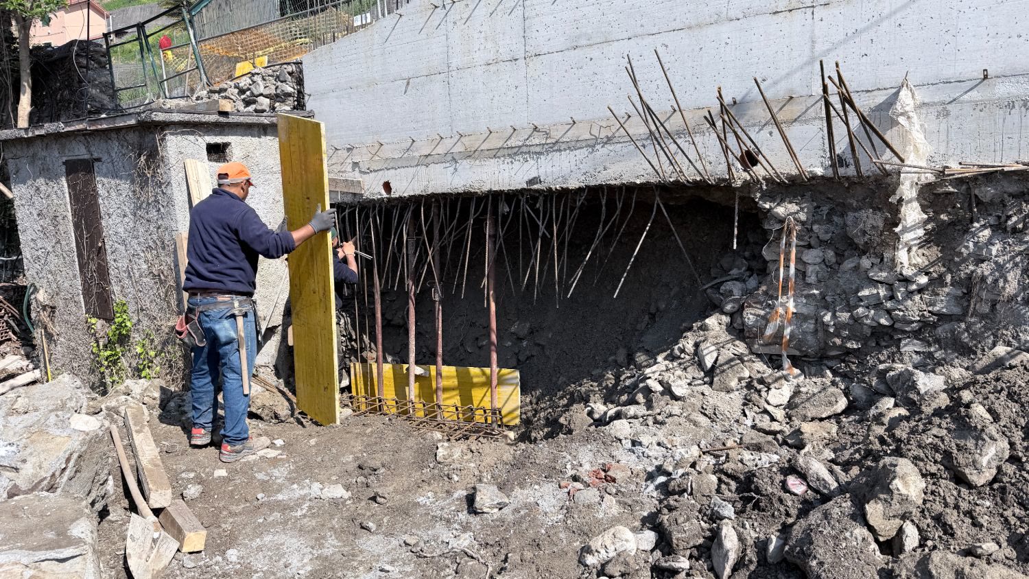 Un operaio monta una cassaforma sotto il muro, fra i ferri d’armatura e lo scavo
