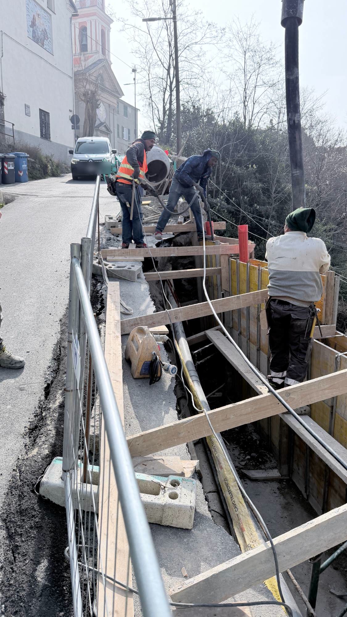 Tre operai dentro le casseforme lungo la strada durante il getto del calcestruzzo, con la chiesa sullo sfondo