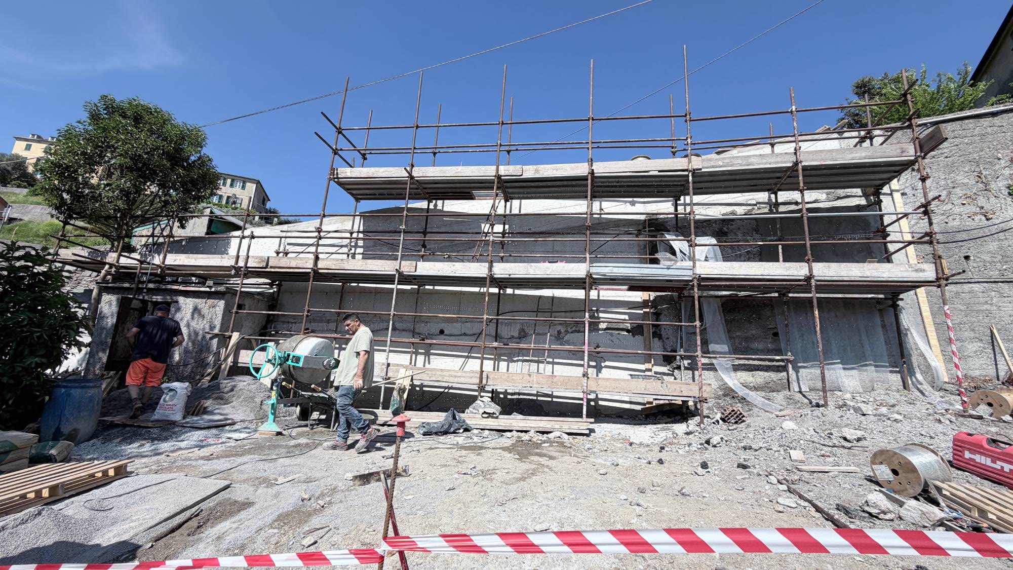 Il nuovo muro in cemento armato sotto il ponteggio, con due operai e la betoniera nel cantiere di Fegino