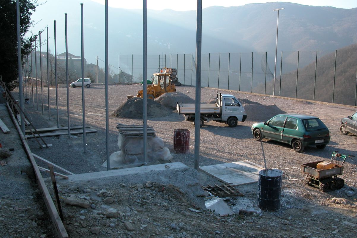 Campo sportivo in terra battuta in costruzione, con i pali della recinzione e le alture sullo sfondo