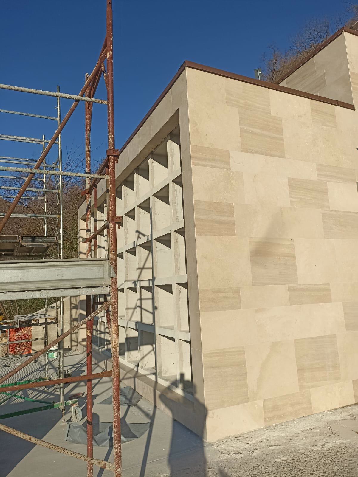 Il fianco del blocco dei loculi rivestito in lastre di pietra chiara, con il ponteggio accanto