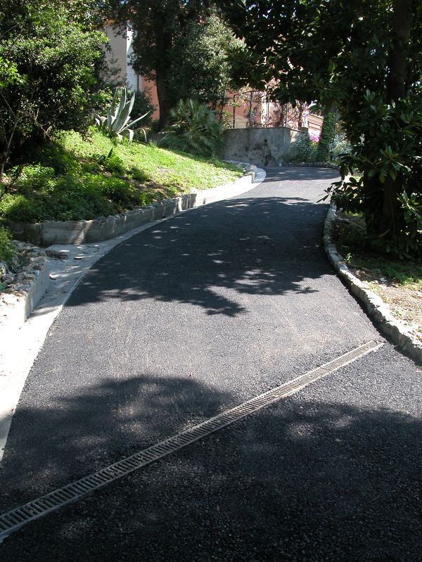 Curva di strada comunale con cunetta in cemento, bordure in grottesco e asfalto nuovo