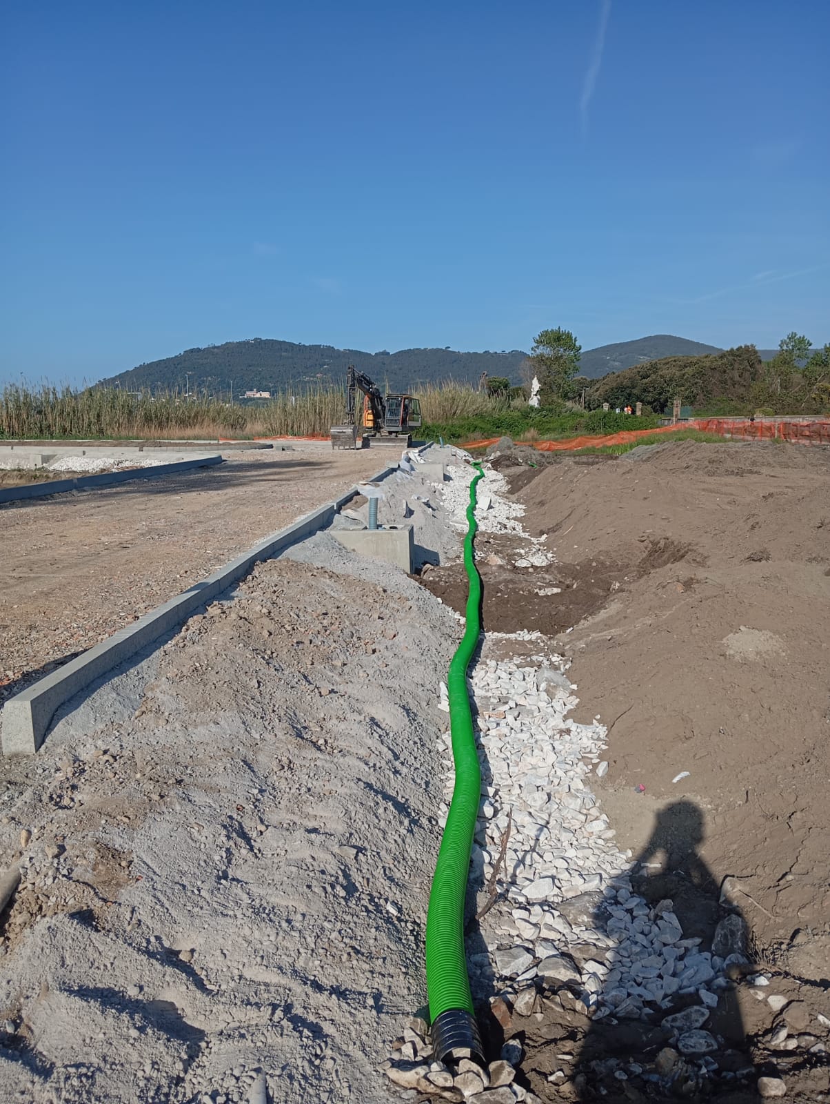 Tubo drenante verde posato su un letto di pietrame bianco lungo il bordo di una strada in costruzione