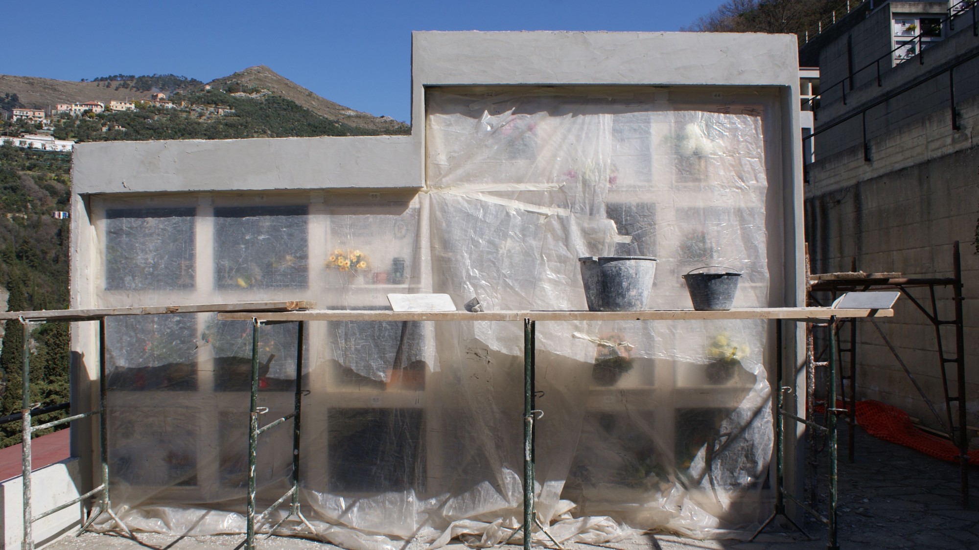 Un blocco di loculi con la cornice appena intonacata; le lapidi sono protette da teli di plastica e davanti c’è il ponteggio