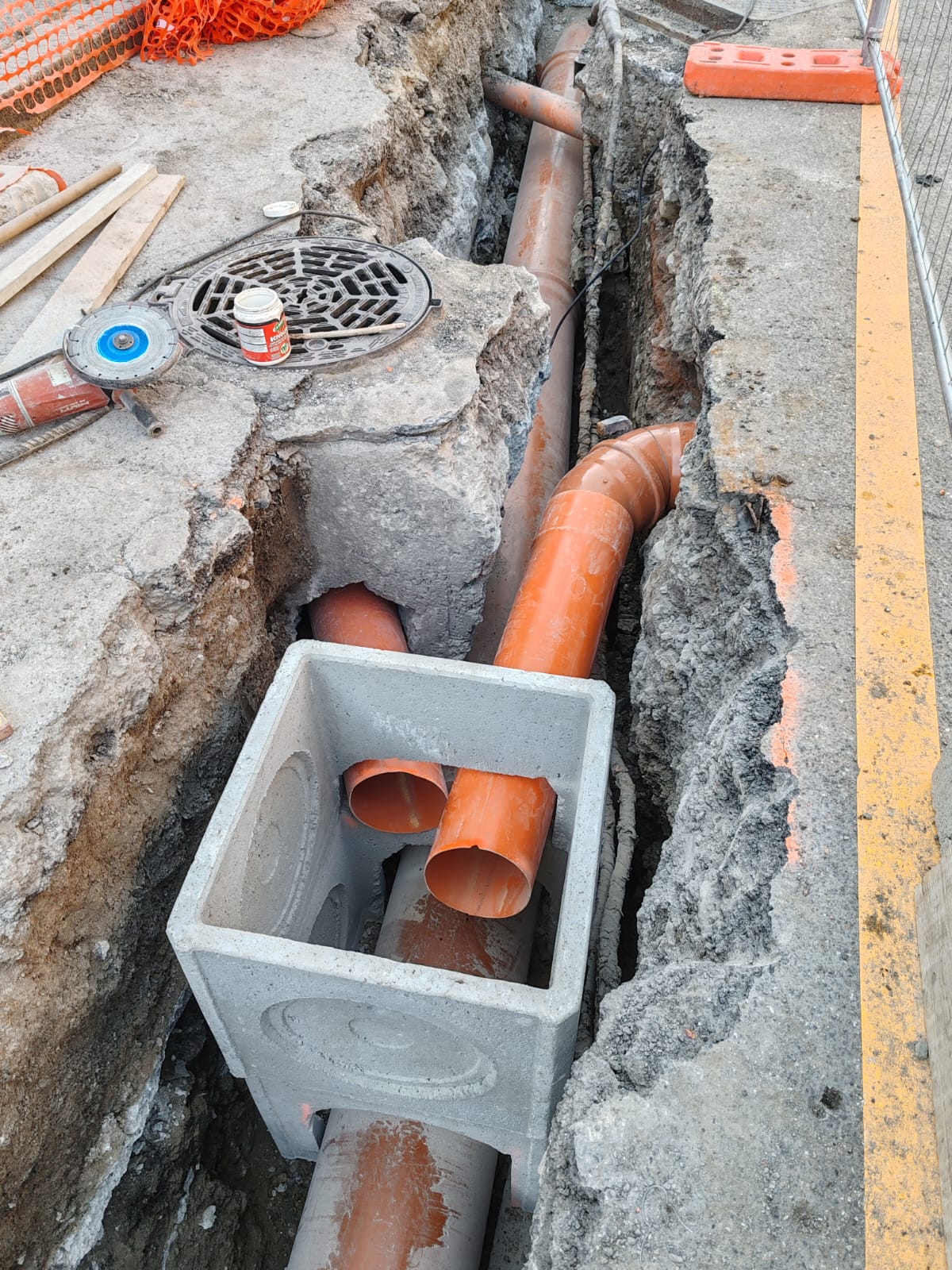 Pozzetto prefabbricato in cemento dentro lo scavo, con le condotte arancioni in PVC che lo attraversano