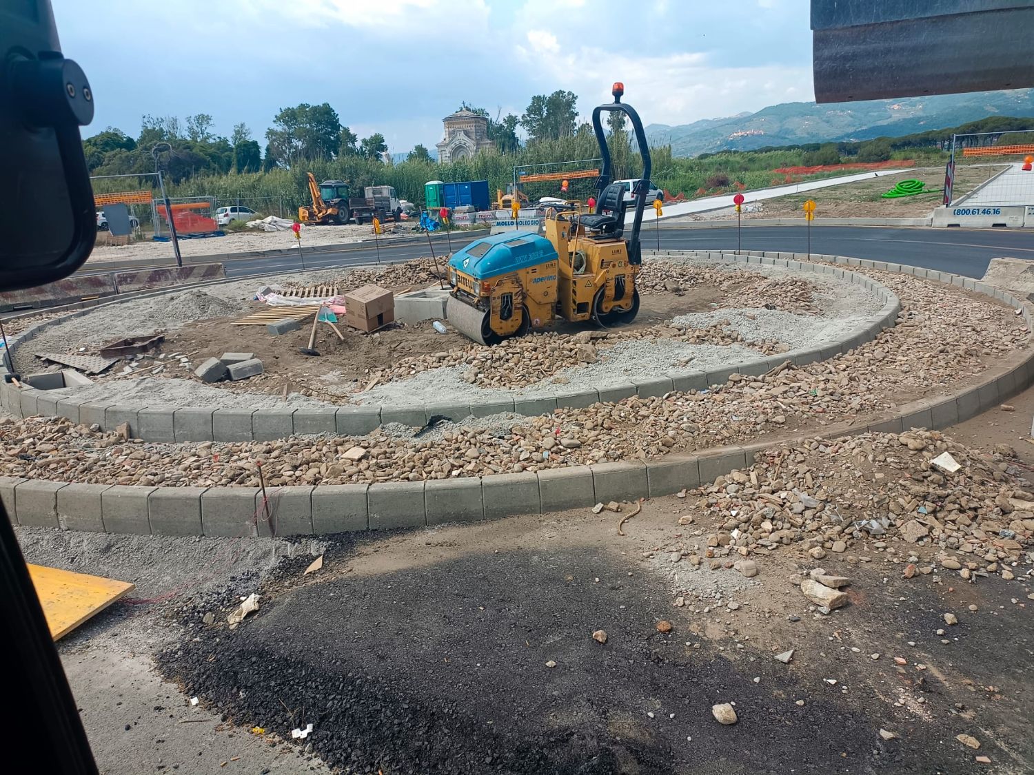 Isola rotatoria in costruzione, con le cordonate in cemento posate e un rullo compattatore al centro