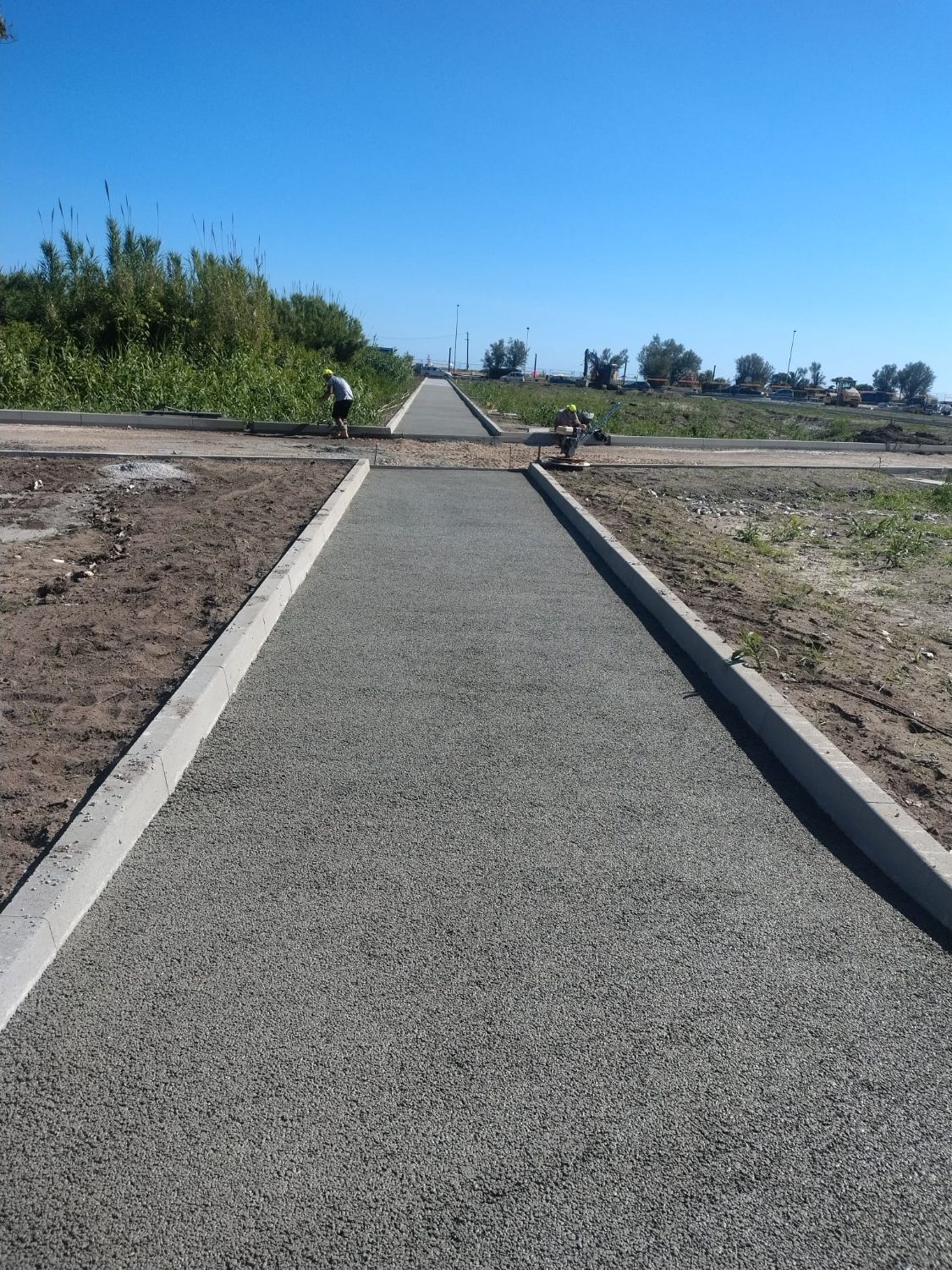 Vialetto pavimentato appena finito fra due cordoli in cemento, con due operai al lavoro sullo sfondo