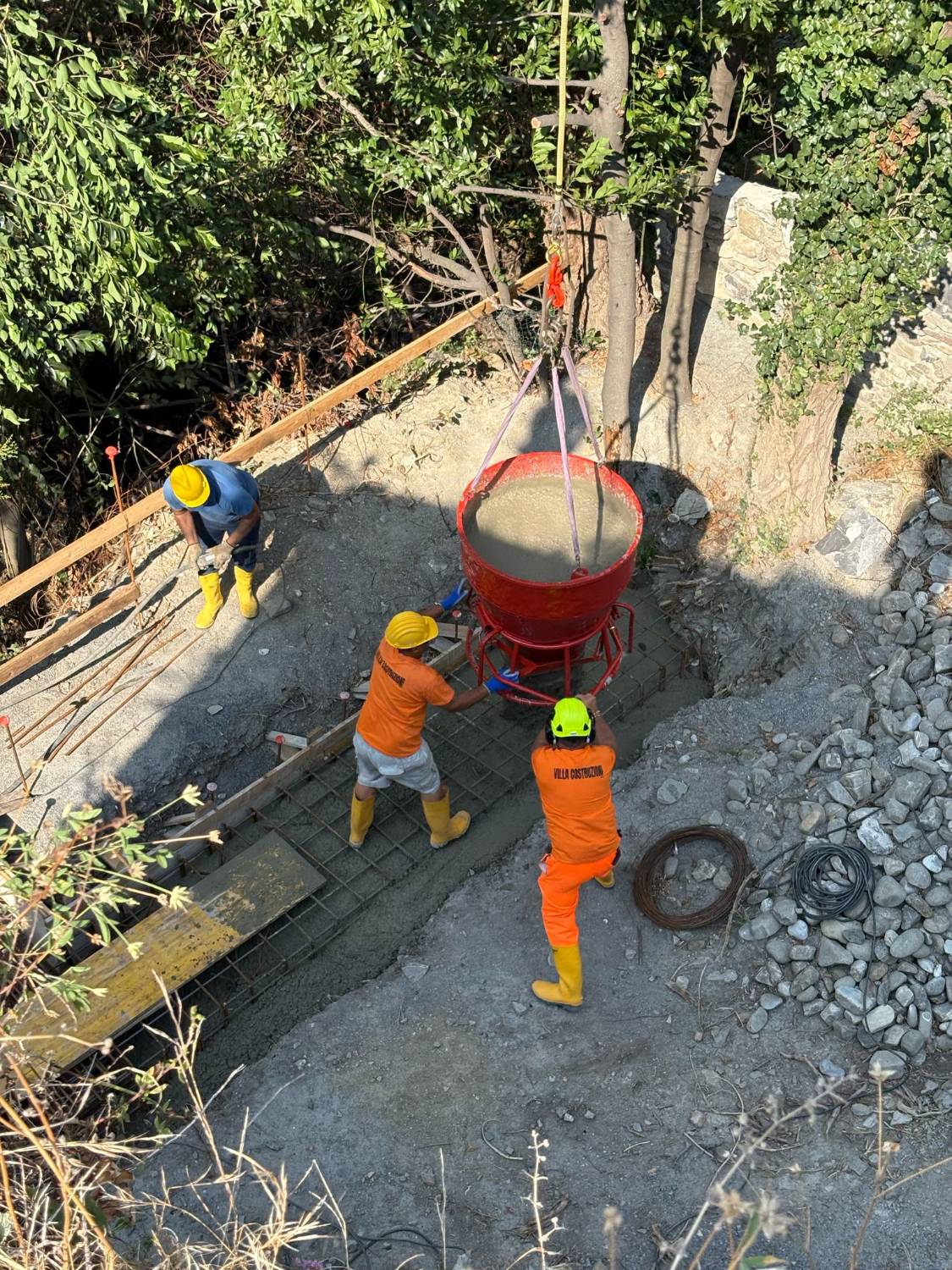 Tre operai guidano la benna del calcestruzzo sopra la rete d’armatura