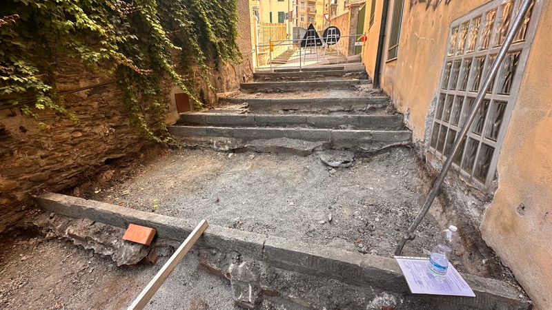 Una rampa della salita con i gradini in pietra e il fondo scavato, fra un muro coperto d’edera e una casa