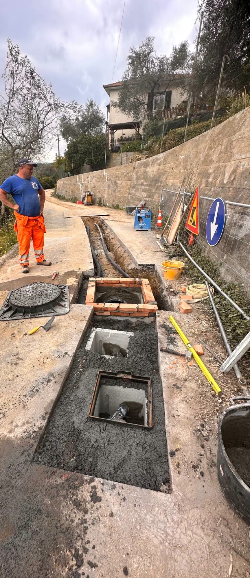I pozzetti lungo la strada prima della posa dei chiusini, con l’operaio e i cartelli del cantiere