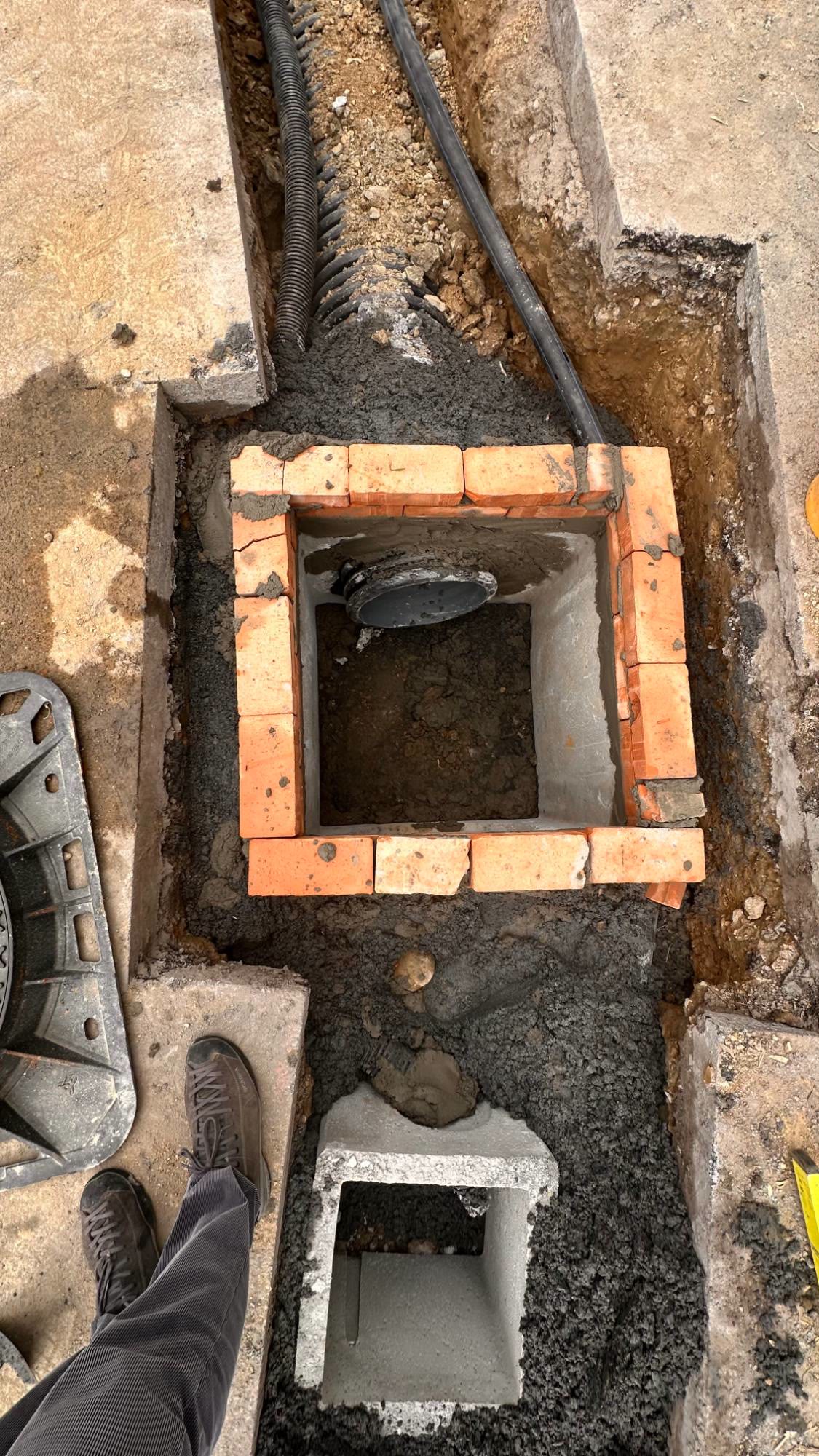 Un pozzetto d’ispezione in mattoni visto dall’alto, con il tubo in PVC e il chiusino in ghisa accanto